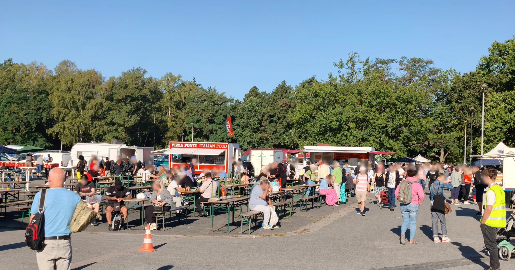 Imbissbereich mit Pizzawagen und besetzten Bierbänken